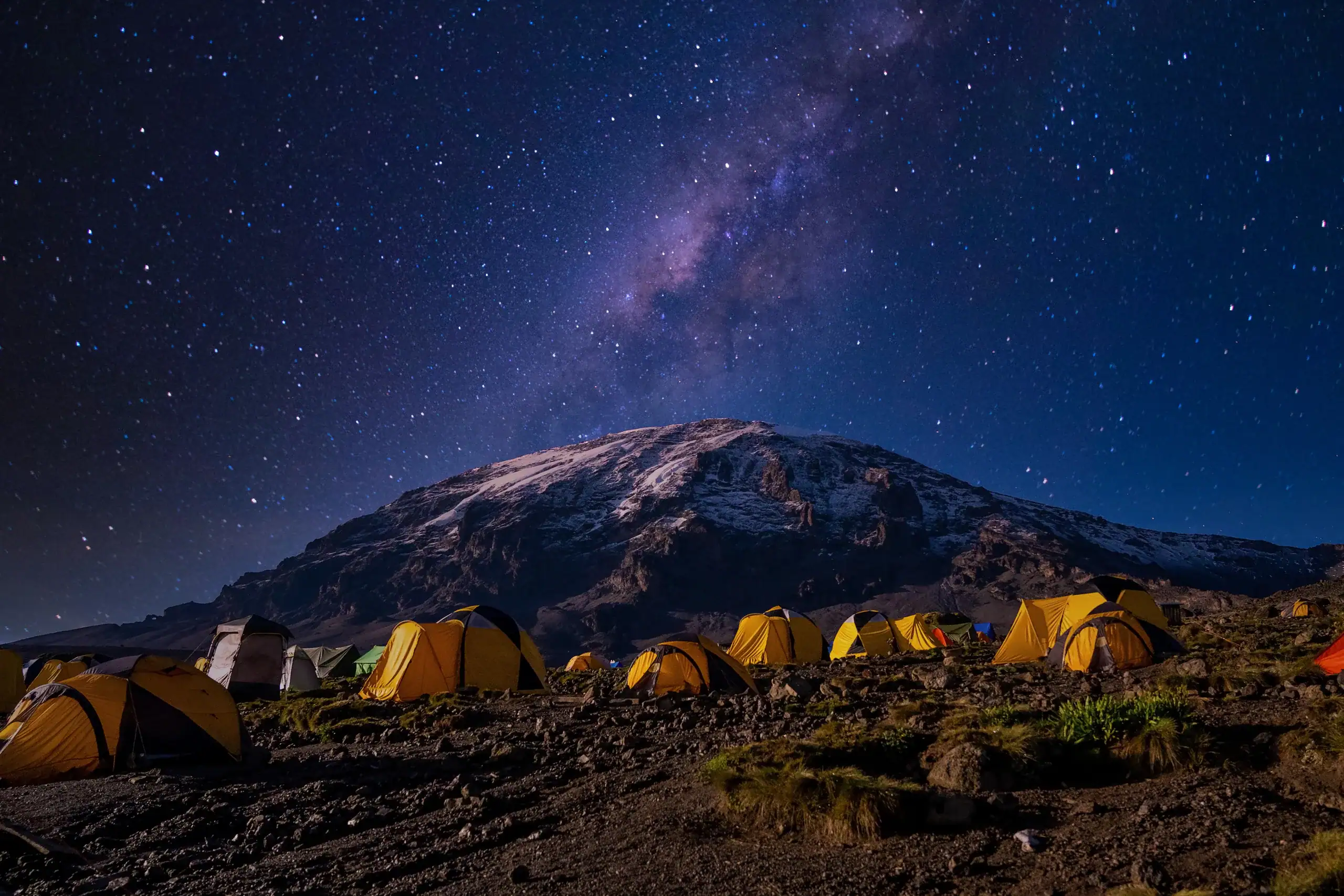 Lit tents of a Kilimanjaro climbing camp beneath the Milky Way and the summit