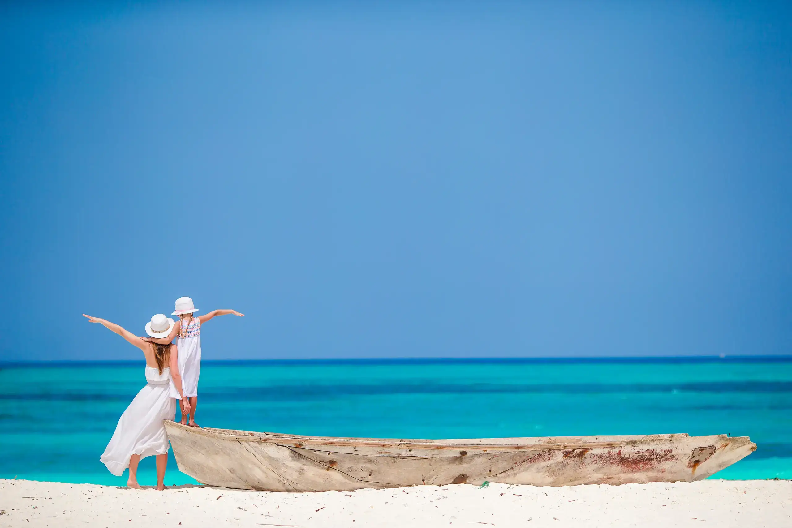 Family standing on a wooden dhow on a white beach