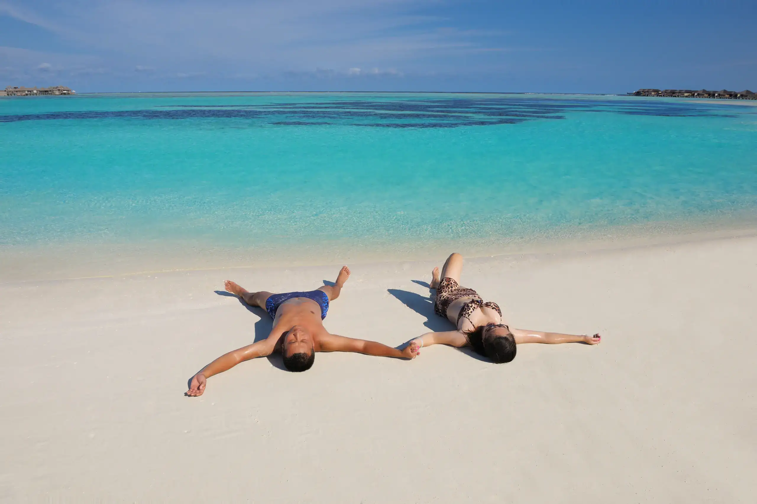 Couple lying on white sand by clear turquoise water
